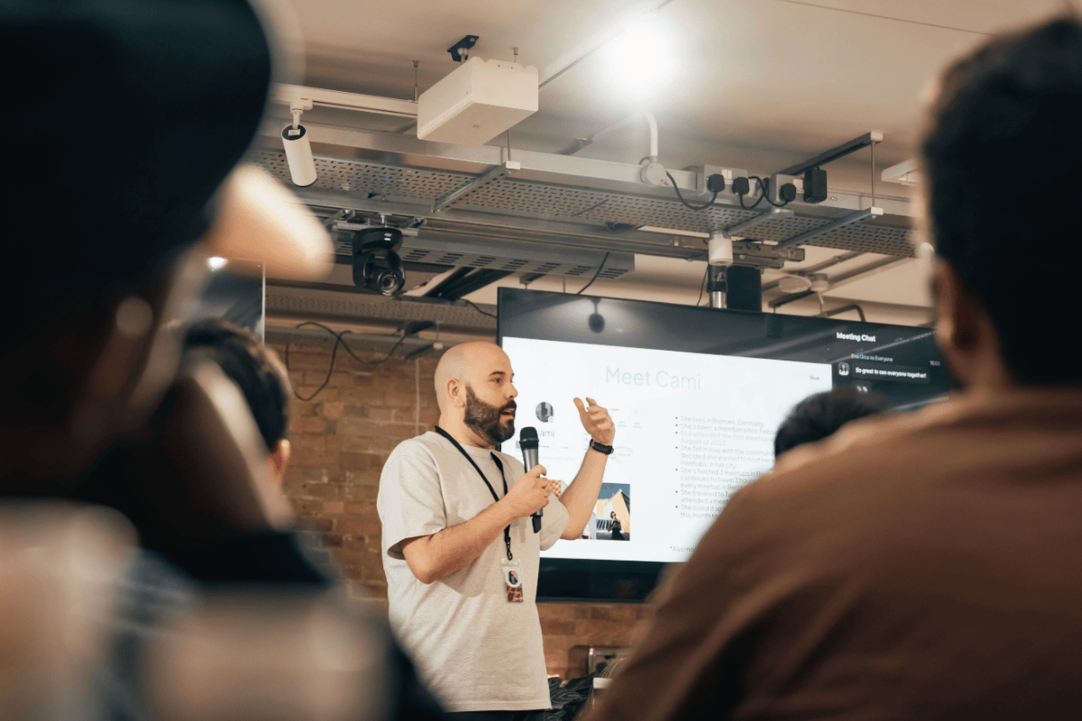 Événement tech : comment créer des échanges qui captivent le public ? 3 Scène de conférence avec un orateur debout sur estrade devant un public attentif, écran géant affichant des graphiques