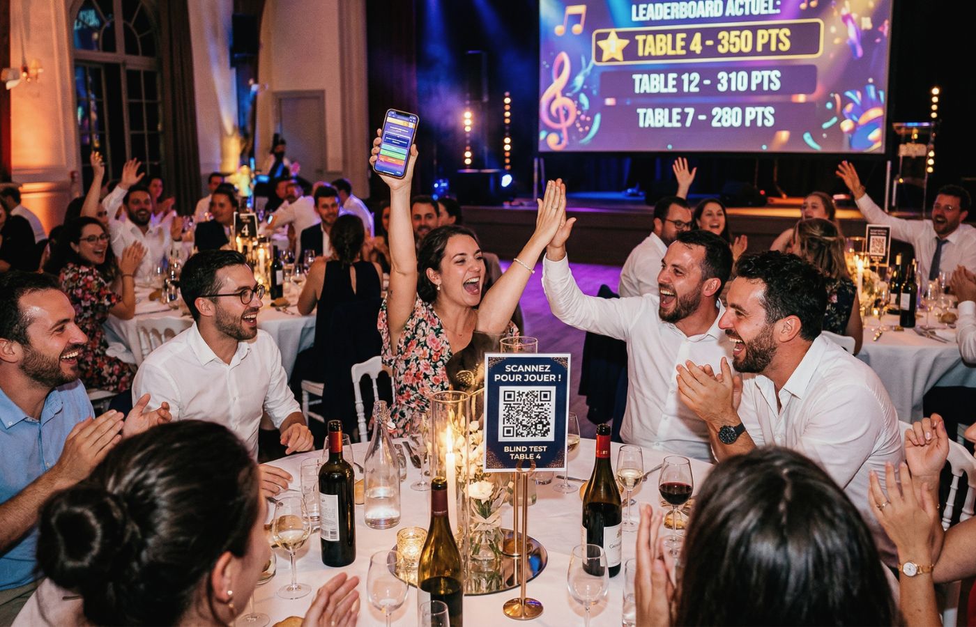 Ambiance festive lors d'un blind test musical par table à un mariage, illustré par des invités scannant un QR code sur leur table pour participer via leur smartphone avec un écran de classement en arrière-plan