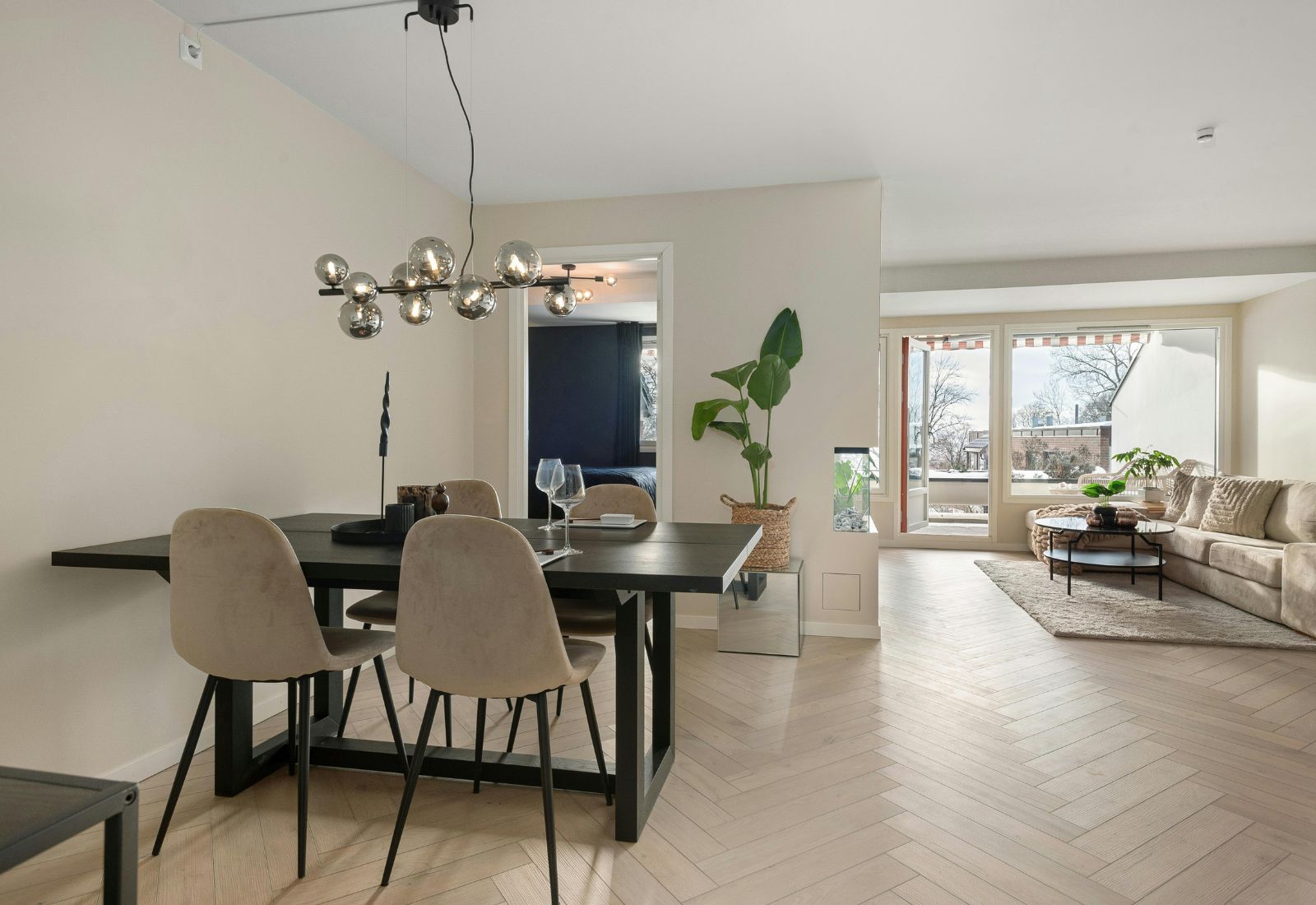 Salle à manger avec suspension multiple à globes en verre fumé sur barre noire, créant un rythme léger dans un espace ouvert.